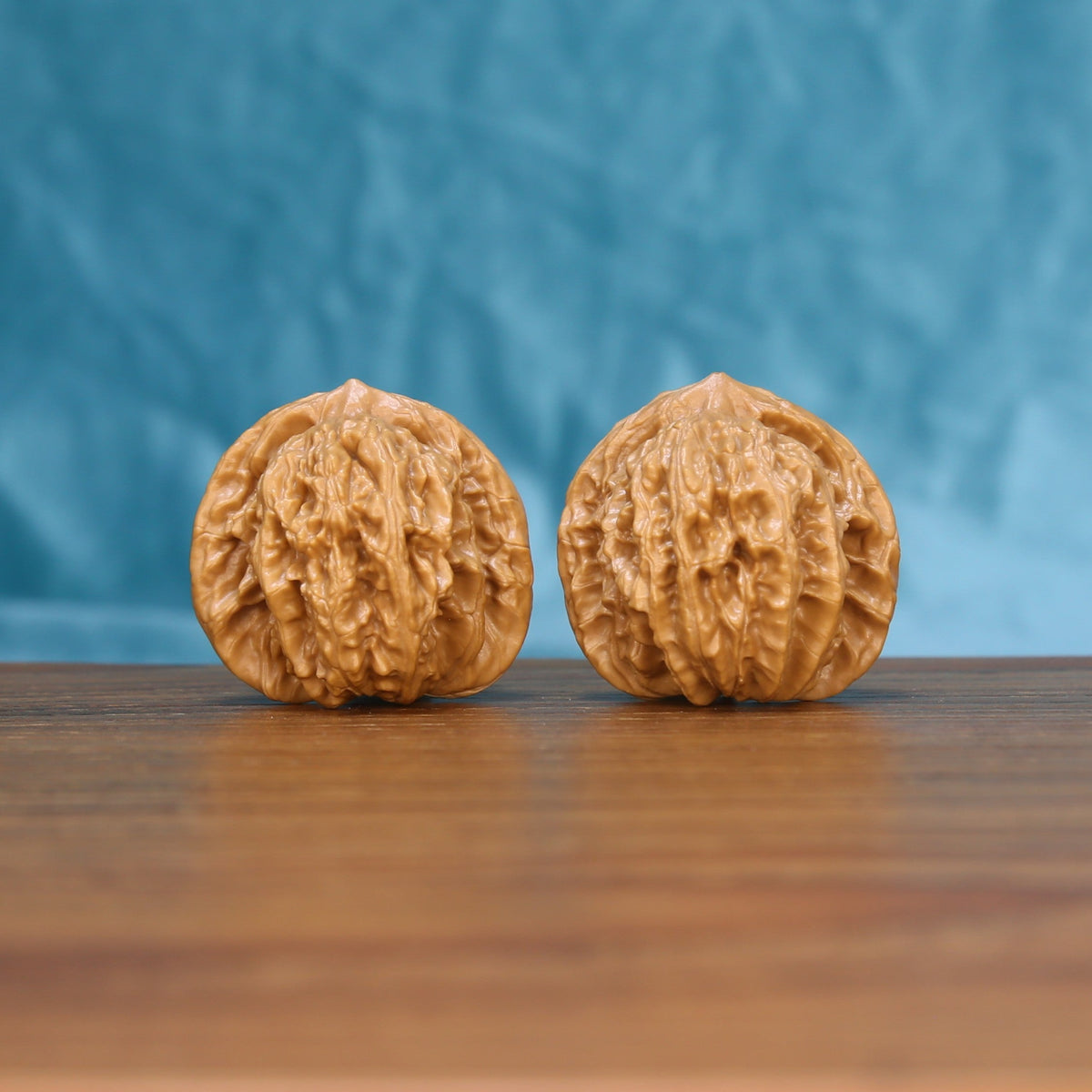 Pair of Coiling Dragon wenwan walnuts carved with dragon relief, displayed on a wood table against a blue background
