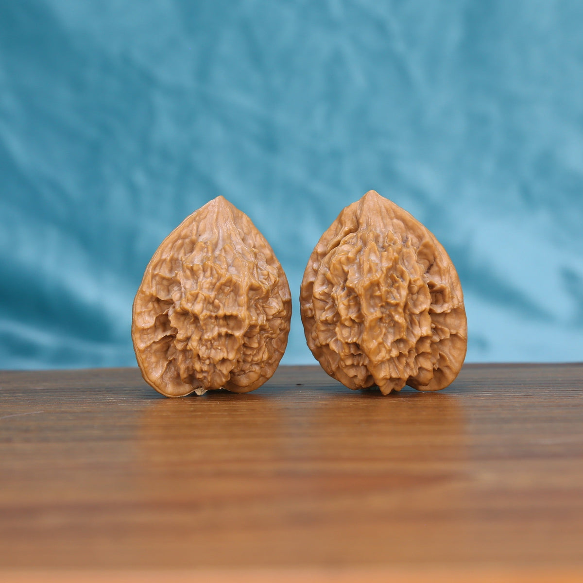 Two Di-Wang wenwan walnuts on wooden surface, blue fabric background – matching spire set