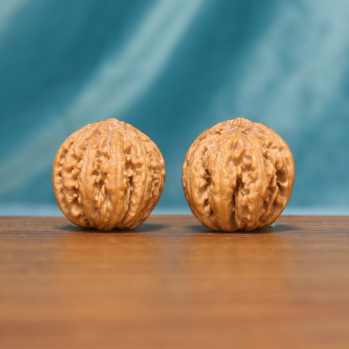 L25 Wenwan walnut matched pair displayed side by side on a wooden surface against a teal background.
