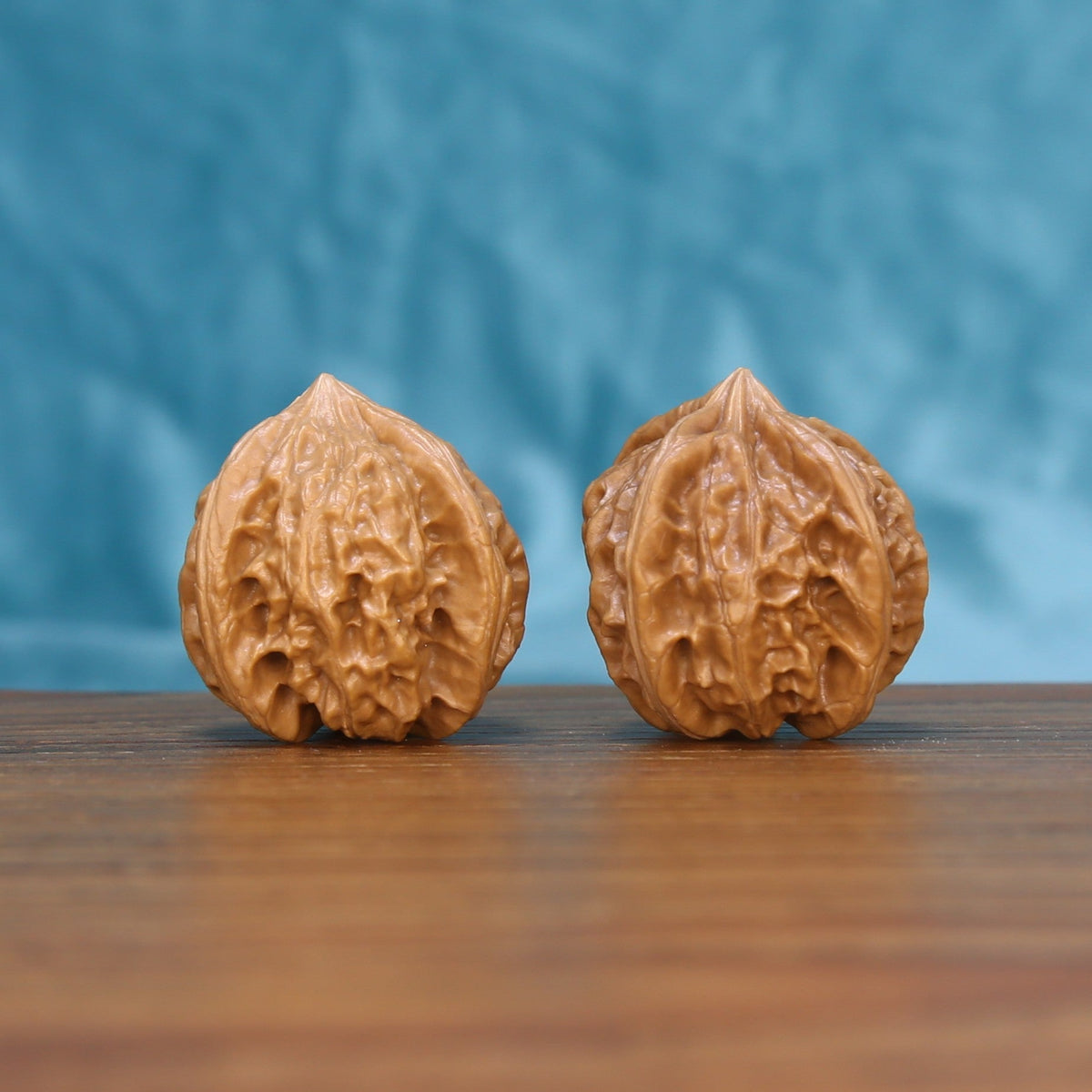 Pair of Four-Ridge Wenwan walnuts standing upright on a wooden surface against a blue background
