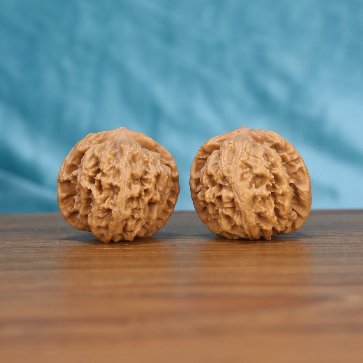 Xing-Tai-Yuan-Bao walnut set side profile on wood, blue background – horizon-curve yuan-bao grain detail