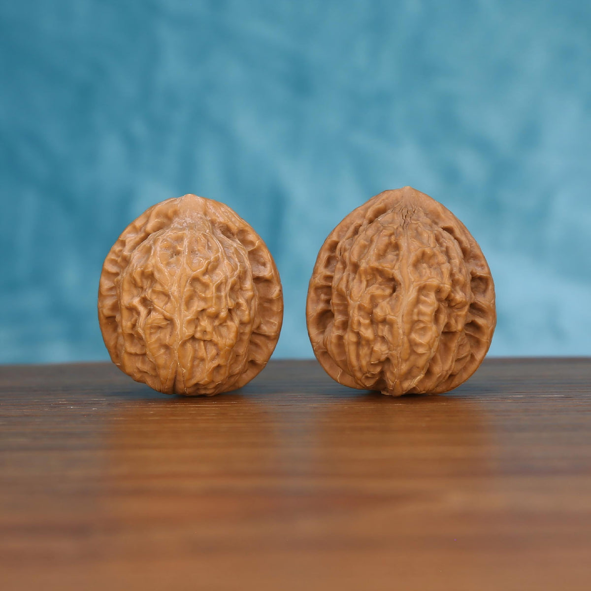 Pair of wenwan walnuts with bold raised ridge pattern and rounded oval form, front view on wooden surface with blue background
