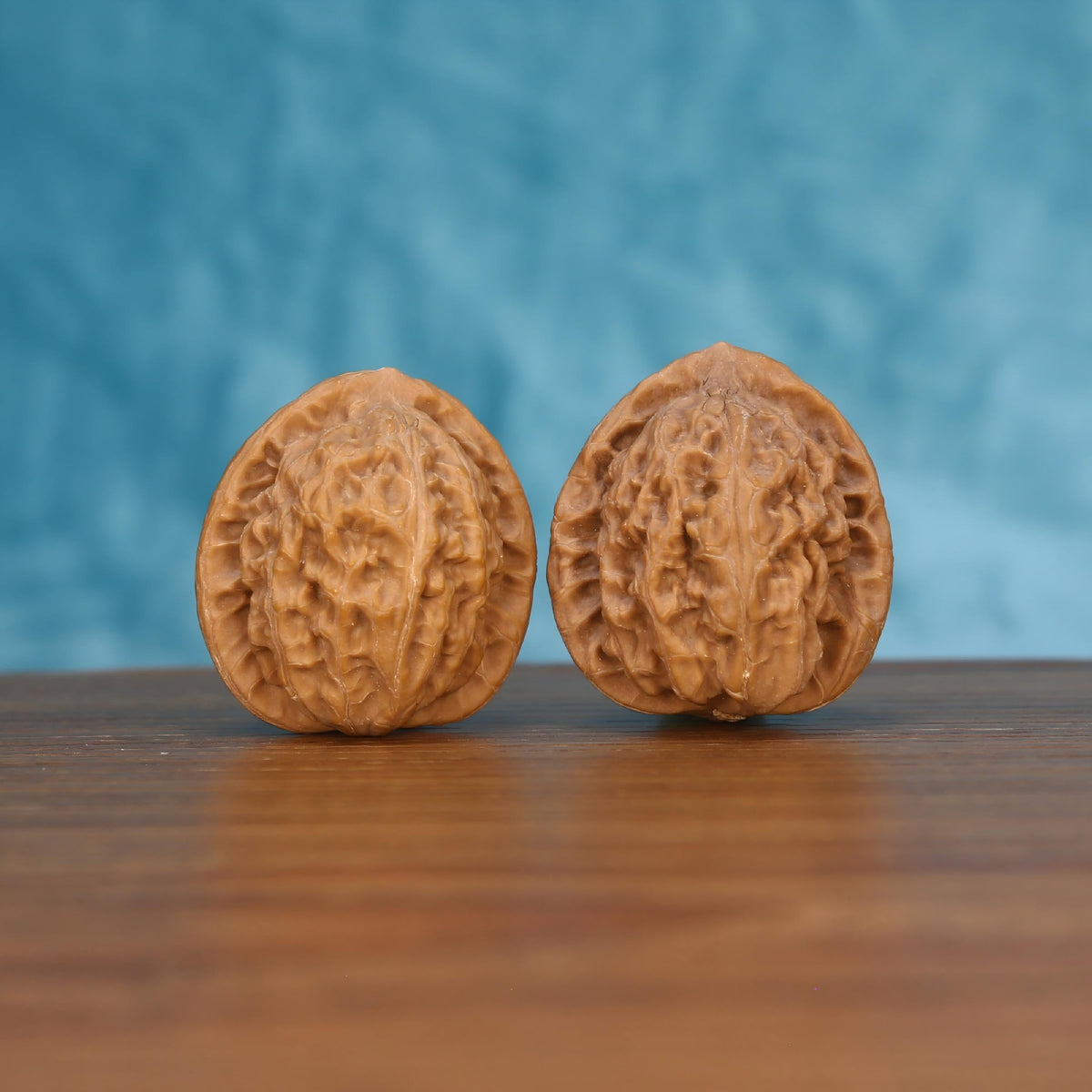 Pair of wenwan walnuts showing deeply wrinkled brain-like surface texture, front view on wooden surface with blue background
