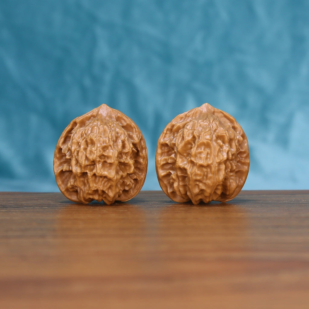 Pair of Linglong Wenwan walnuts standing upright on a wooden surface against a blue background
