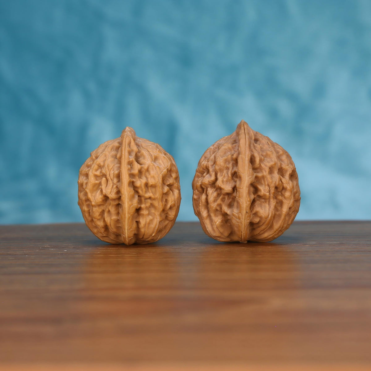 Pair of wenwan walnuts with prominent vertical seam and intricate carved surface, upright front view on wooden surface with blue background
