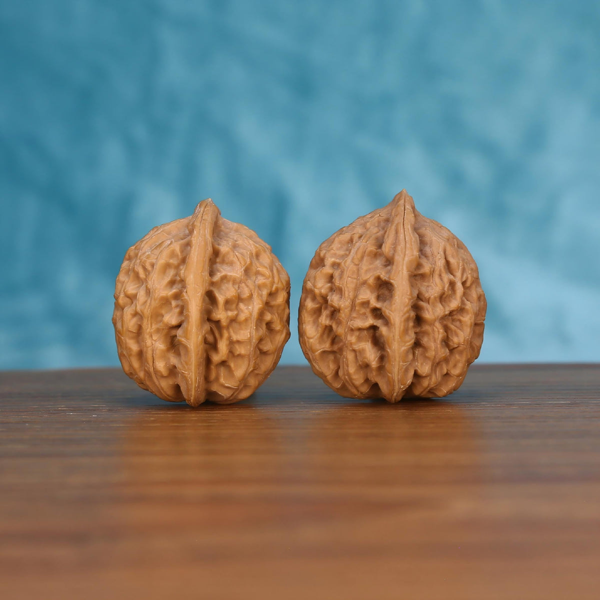 Pair of wenwan walnuts with sharp pointed tip and deep leaf-vein ridge pattern, front view on wooden surface with blue background
