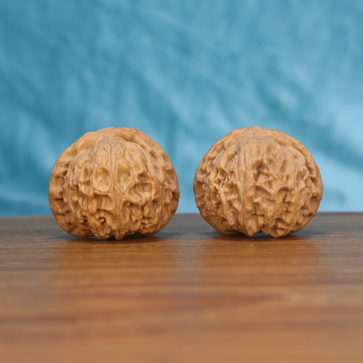 Two Gong-Deng wenwan walnuts on wooden surface, blue fabric background – matching imperial set
