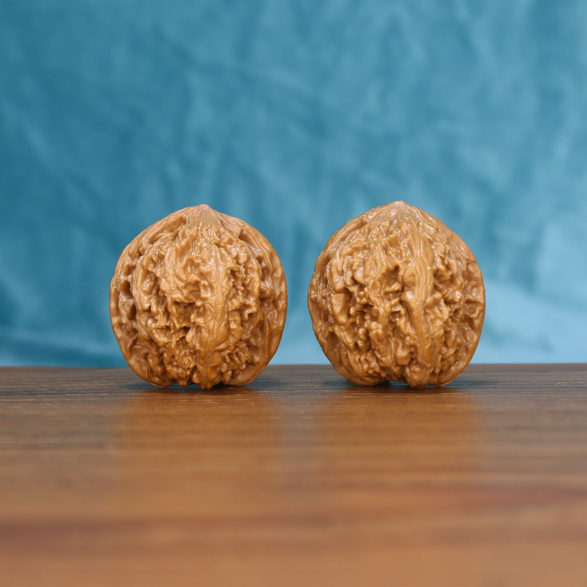 Pair of Stone Wenwan walnuts standing upright on a wooden surface against a blue background
