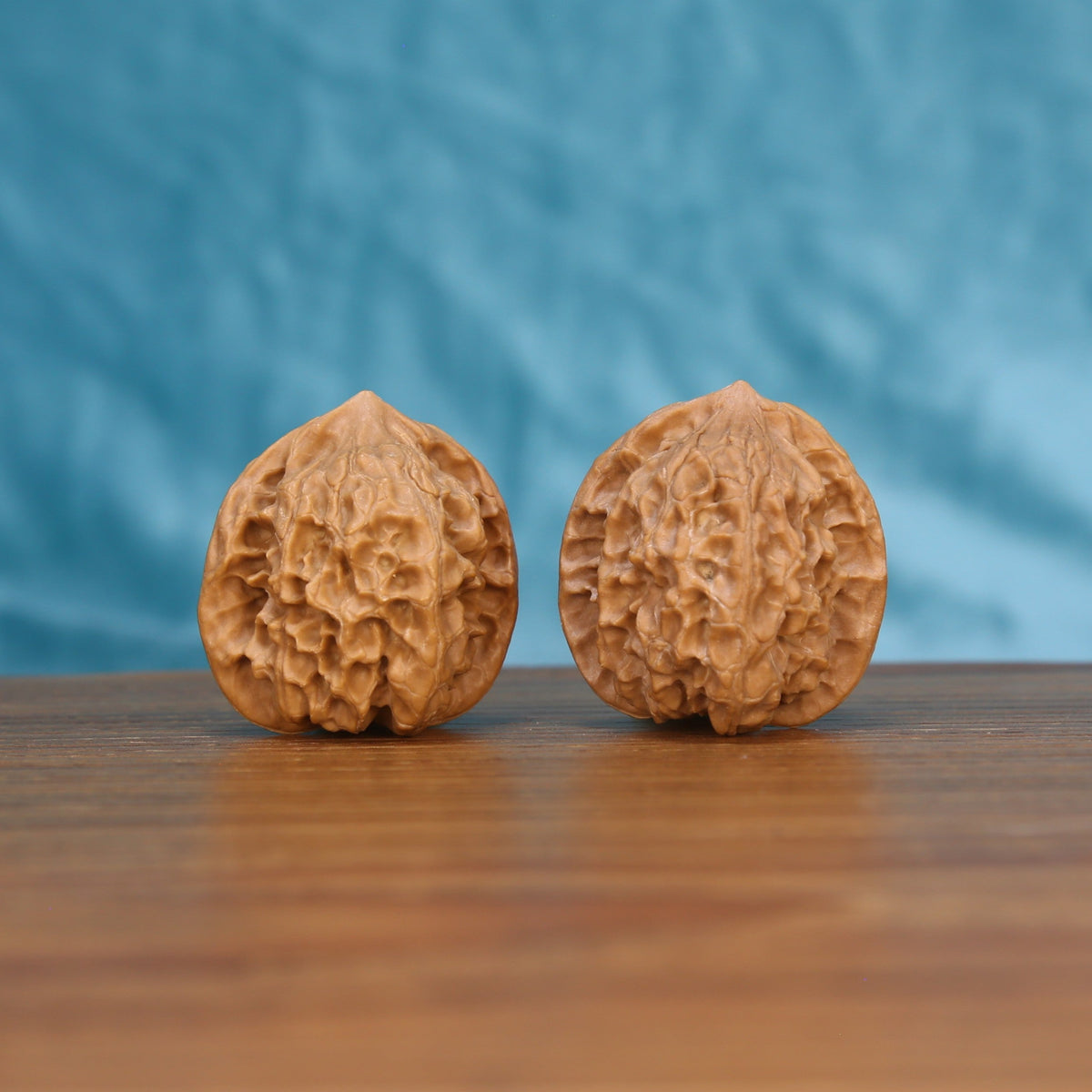 Two Ling-Long wenwan walnuts on wooden surface, blue fabric background – matching carved labyrinth set