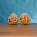 Pair of Emperor wenwan walnuts with tall pointed form and deep relief carving on a wood table against a blue background
