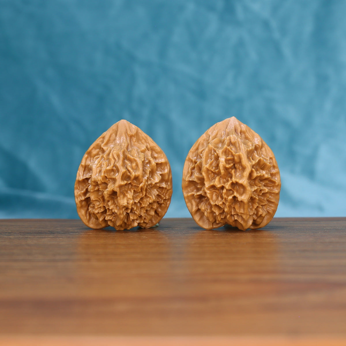 Pair of Emperor wenwan walnuts with tall pointed form and deep relief carving on a wood table against a blue background
