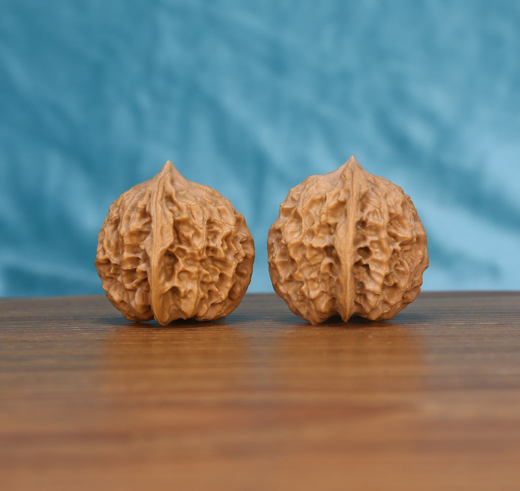 Ling-Long wenwan walnut pair alternate angle, blue background – symmetrical carved labyrinth ridge pattern