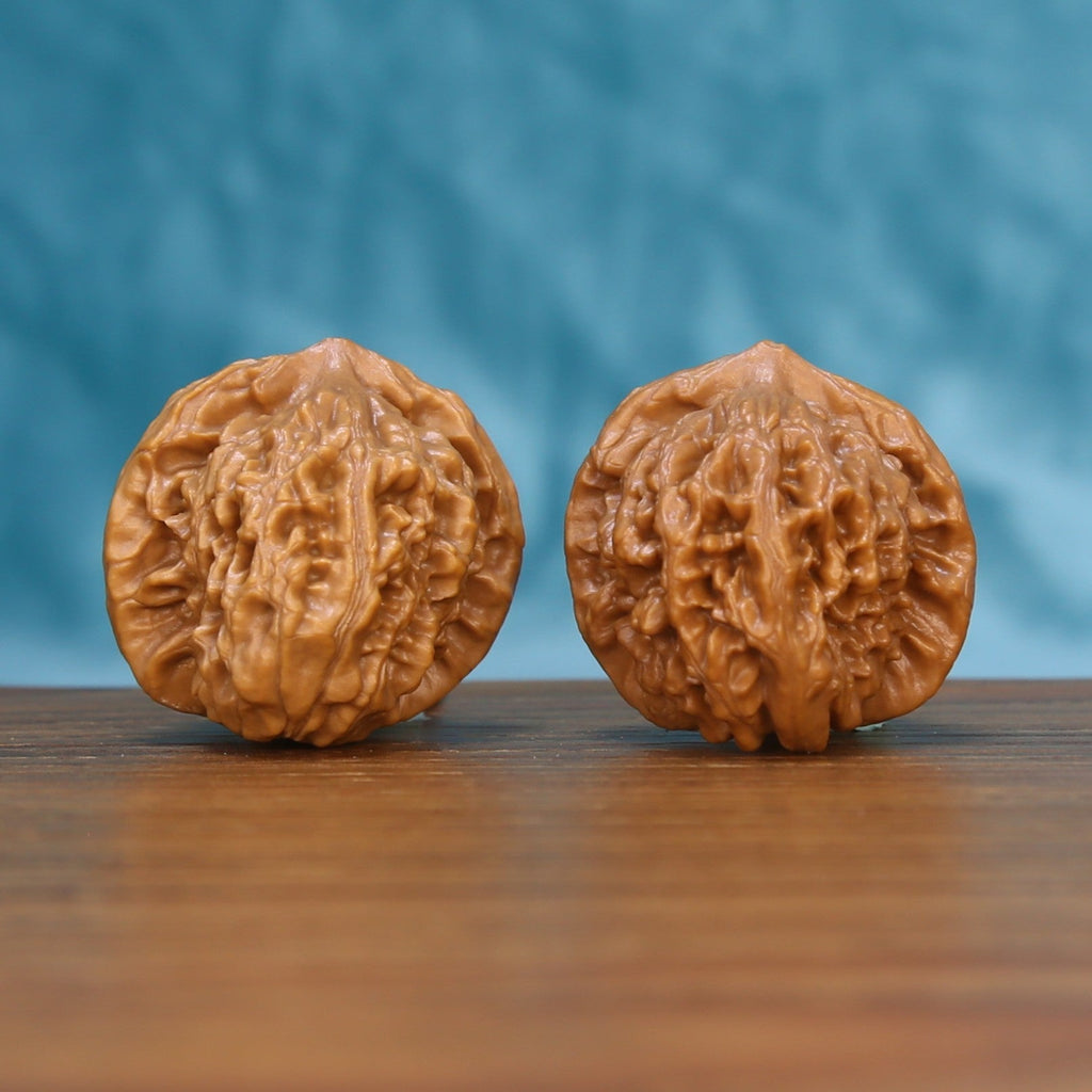 Pair of Qinhuangdao Yuanbao Wenwan walnuts standing upright on a wooden surface against a blue background
