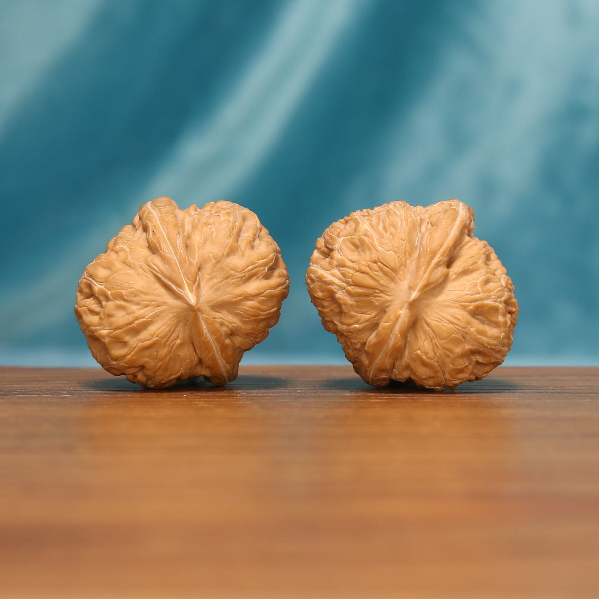 L16 Wenwan walnut pair shown from the side, highlighting radiating ridges and sculpted shell surfaces.
