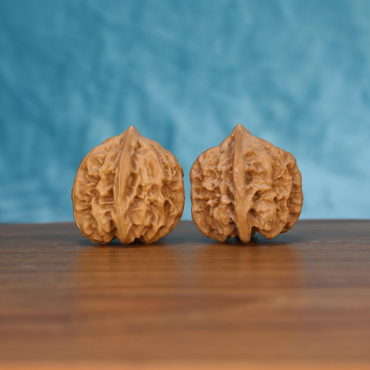 Pair of wenwan walnuts with coarsely pitted open wrinkled surface and wide squat rounded form, front view on dark velvet surface with black background
