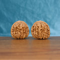 Pair of Sizuo Lou Wenwan walnuts standing upright on a wooden surface against a blue background
