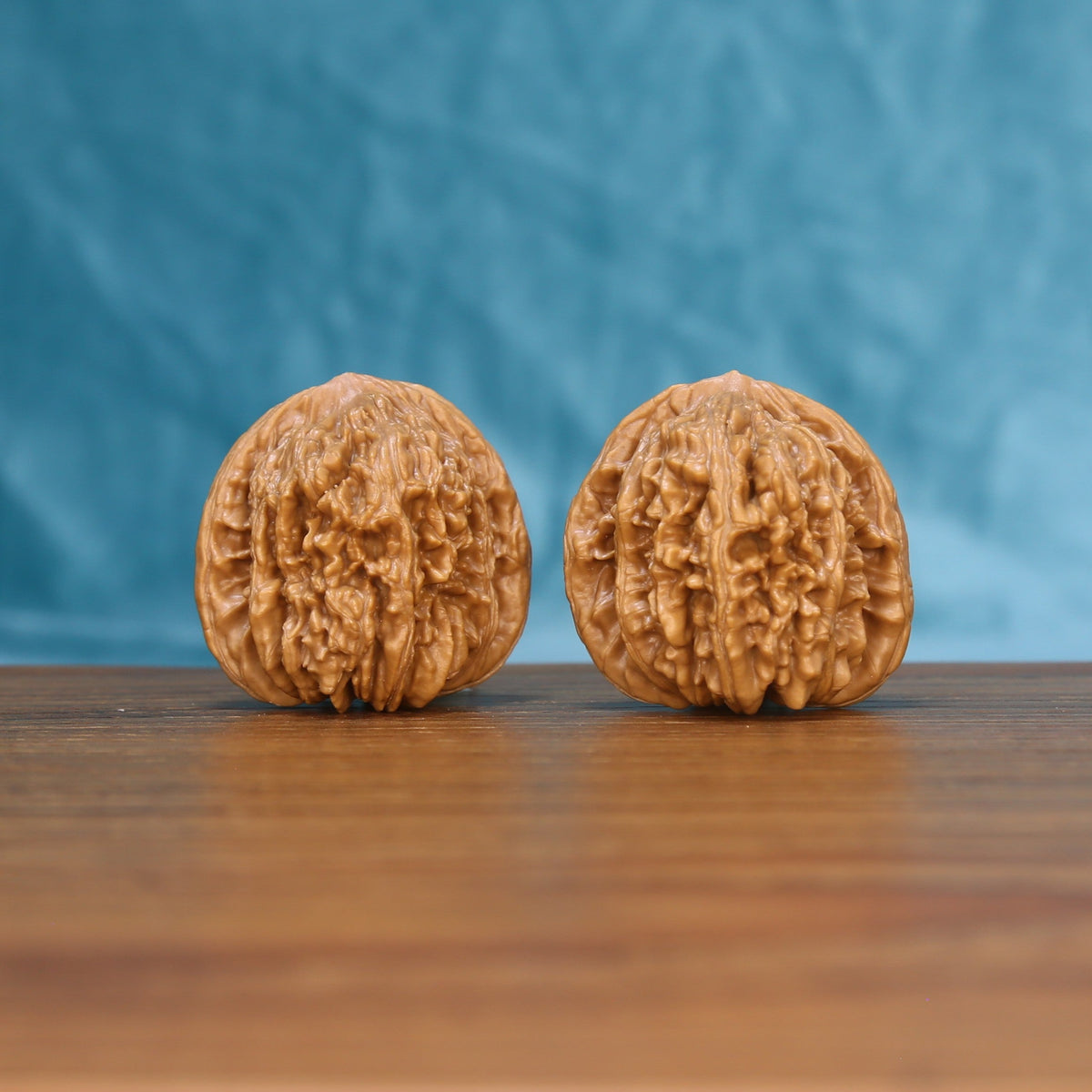 Pair of Sizuo Lou Wenwan walnuts standing upright on a wooden surface against a blue background
