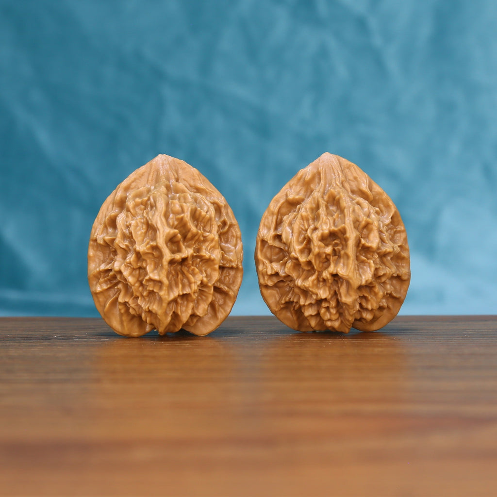 Pair of Emperor wenwan walnuts with tall peach-shaped form and deep relief carving on a wood table against a blue background

