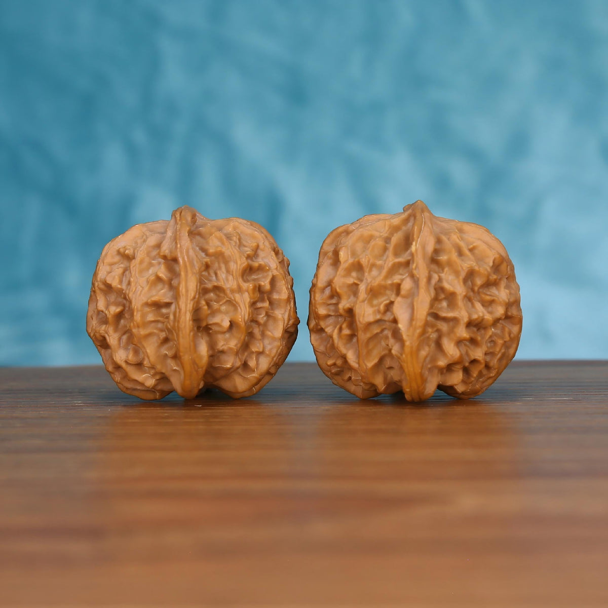 Pair of wenwan walnuts with deep carved grooves and bold vertical seam, front view on wooden surface with blue background
