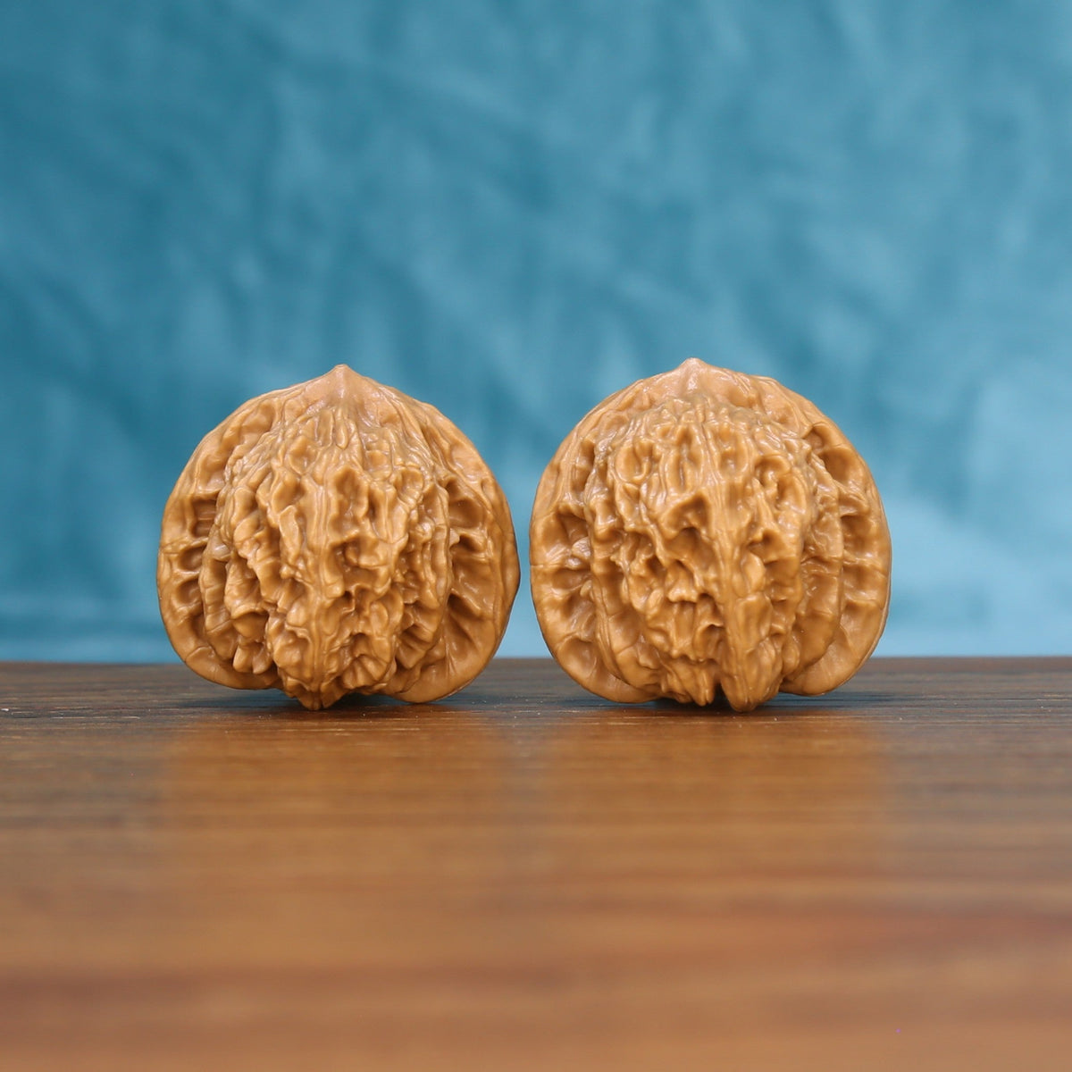 Pair of Coiling Dragon Wenwan walnuts standing upright on a wooden surface against a blue background
