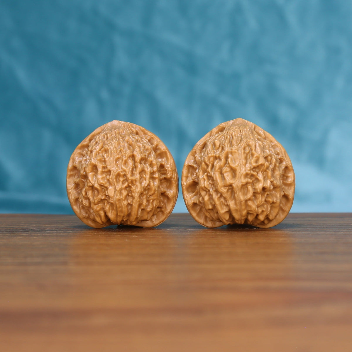 Pair of Little Golden Ox wenwan walnuts with tall narrow form and fine ridge carving on a wood table against a blue background
