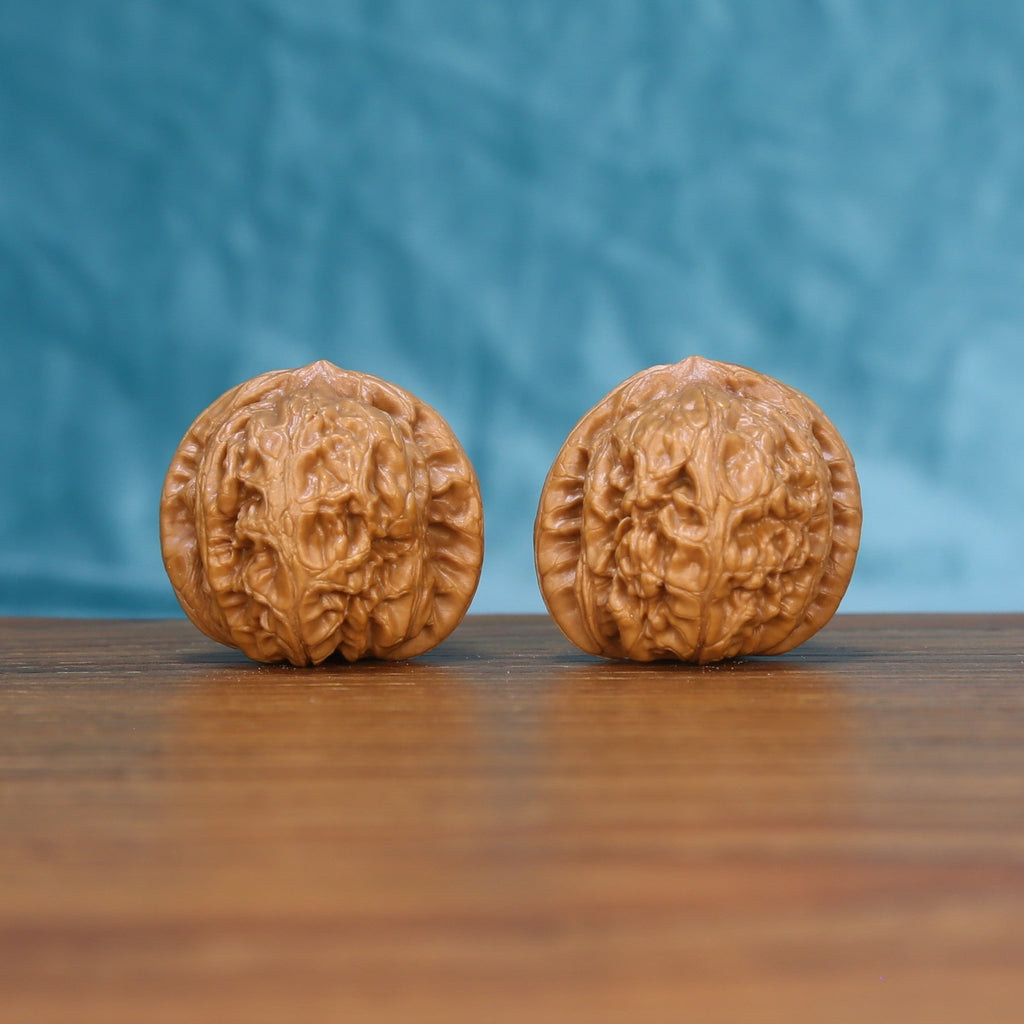 Pair of Pinggu Ingot wenwan walnuts with rounded ingot shape and dense ridge carving on a wood table against a blue background

