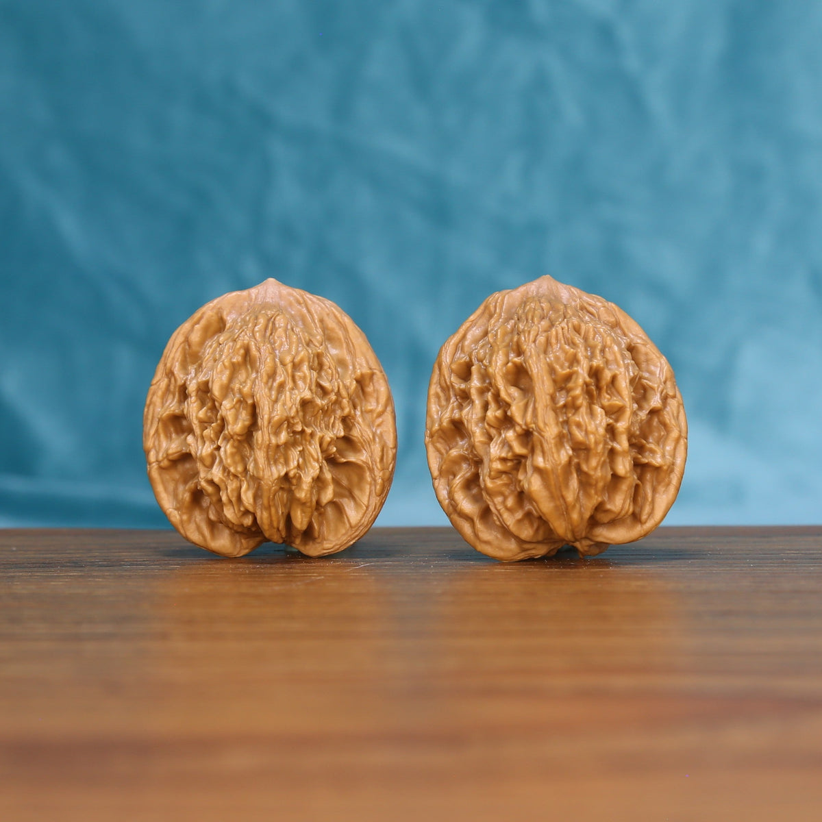 Pair of Wheat Tiger Wenwan walnuts standing upright on a wooden surface against a blue background
