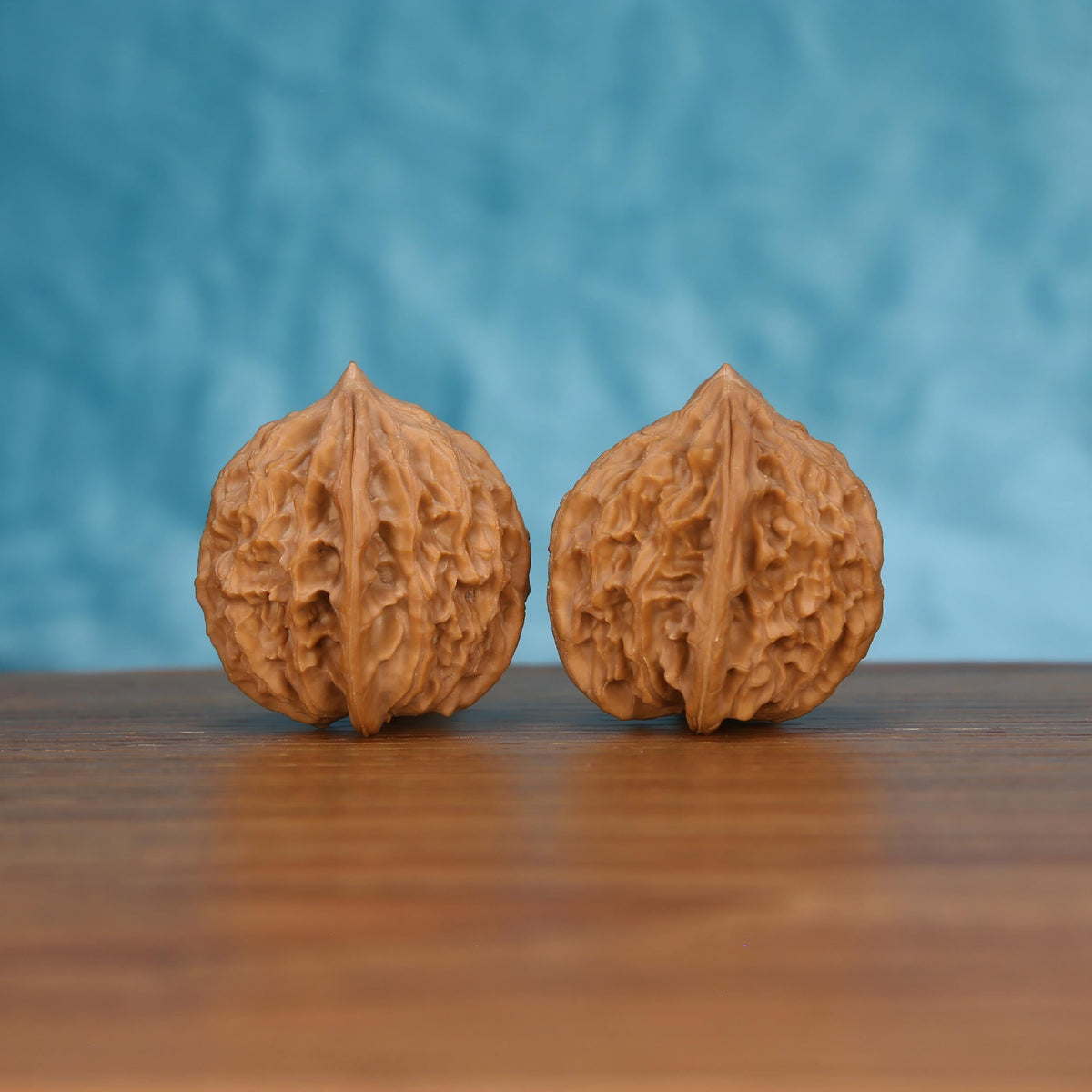 Pair of wenwan walnuts with deep carved grooves and pointed tip, front view on wooden surface with blue background
