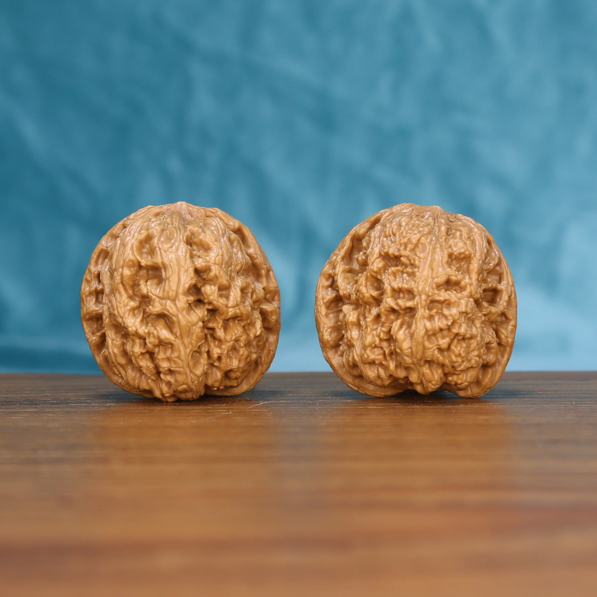 Pair of General wenwan walnuts with bold high-relief ridges on a wood table against a blue background
