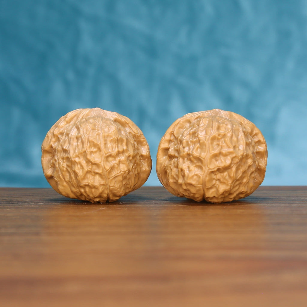 Pair of pumpkin-shaped wenwan walnuts with deep ridged texture on a wood table against a blue background
