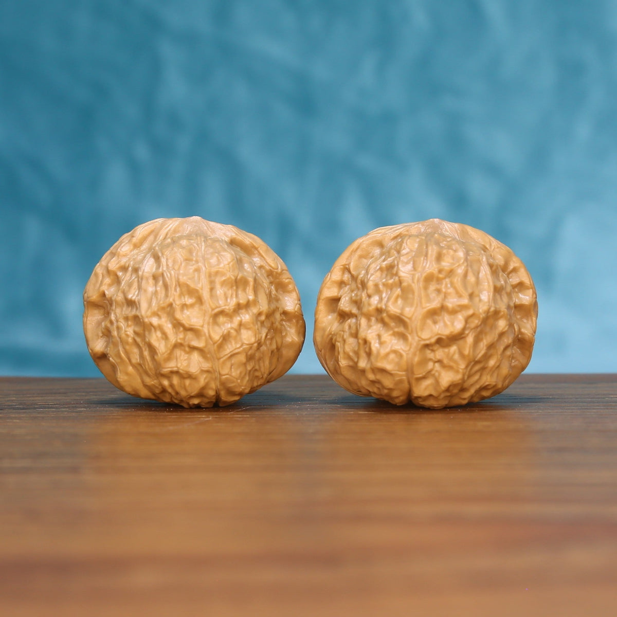 Pair of pumpkin-shaped wenwan walnuts with deep ridged texture on a wood table against a blue background
