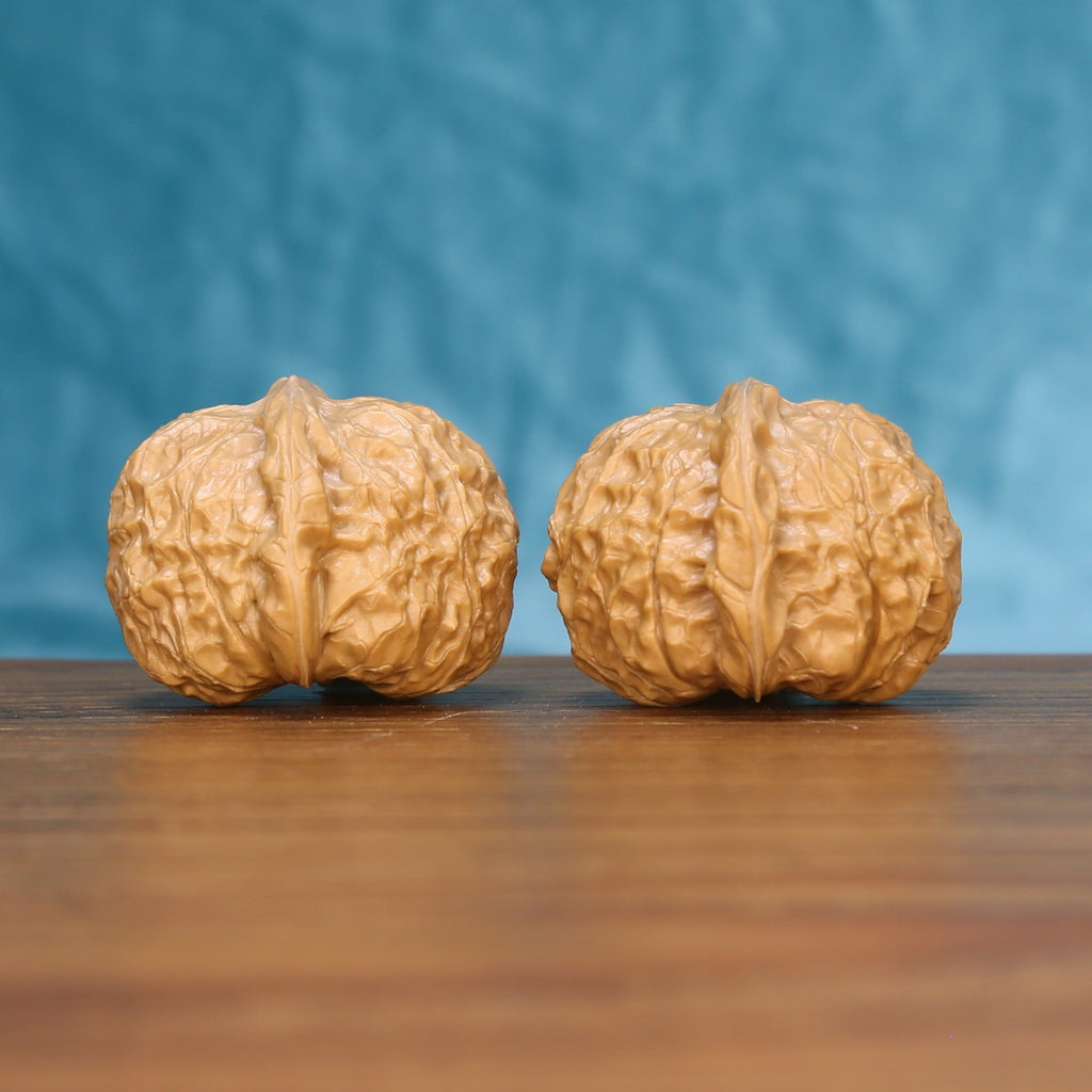Close view of two matched pumpkin wenwan walnuts showing dense ridge carving and golden natural grain
