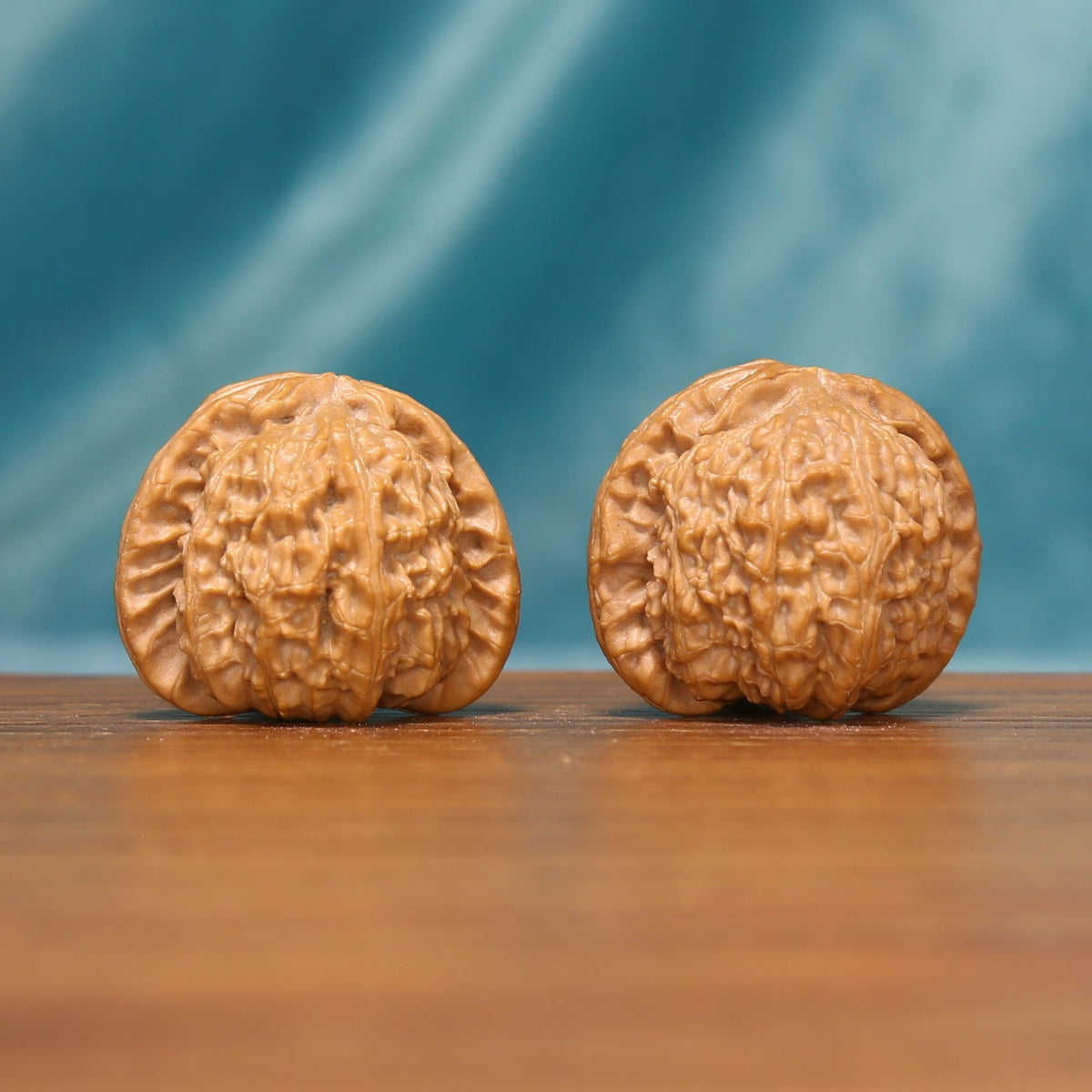 Front view of a Tiger Head Wenwan walnut pair with rounded forms and dense natural ridges on a wooden surface.
