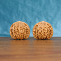 Pair of Coiling Dragon Wenwan walnuts standing upright on a wooden surface against a blue background
