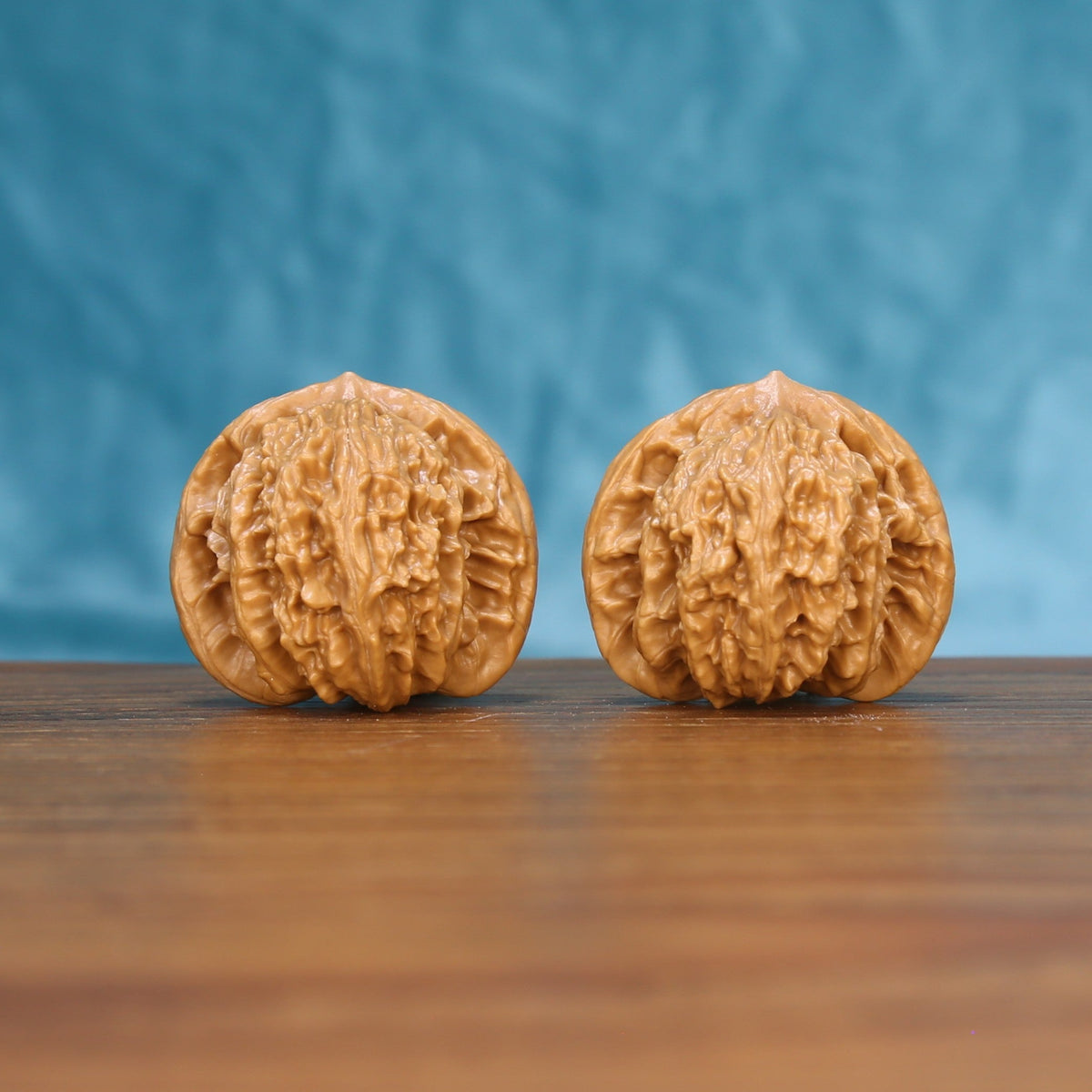 Pair of Coiling Dragon Wenwan walnuts standing upright on a wooden surface against a blue background
