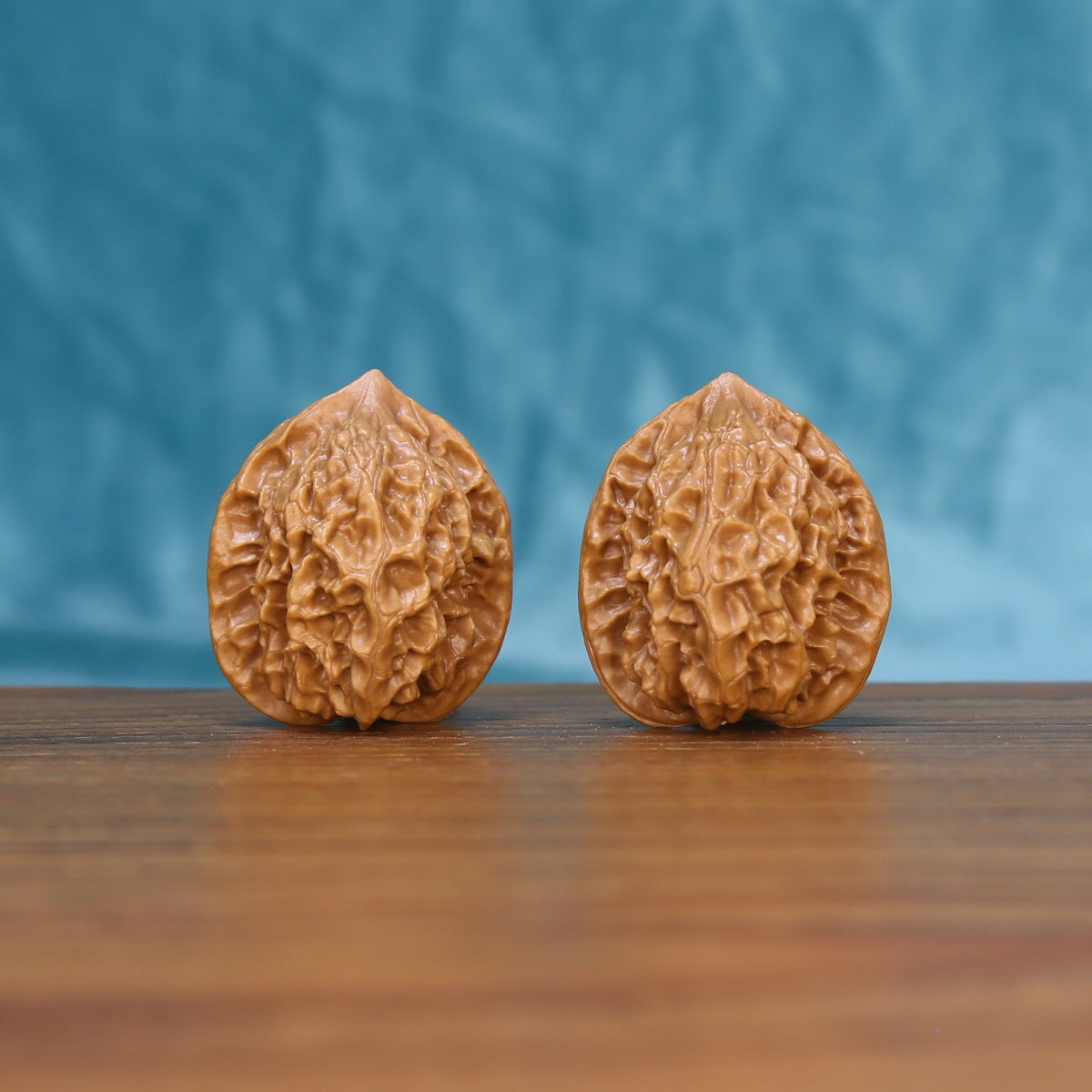 Pair of Linglong Wenwan walnuts standing upright on a wooden surface against a blue background
