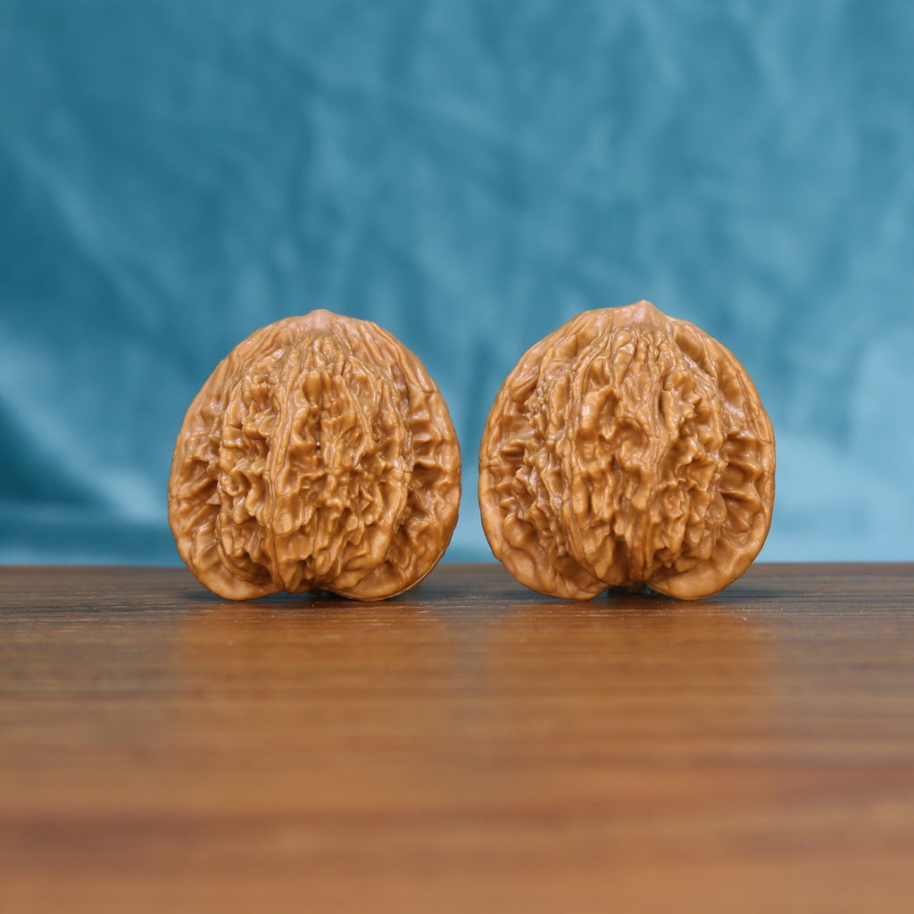 Pair of Wheat Tiger wenwan walnuts with round body and dense relief carving on a wood table against a blue background
