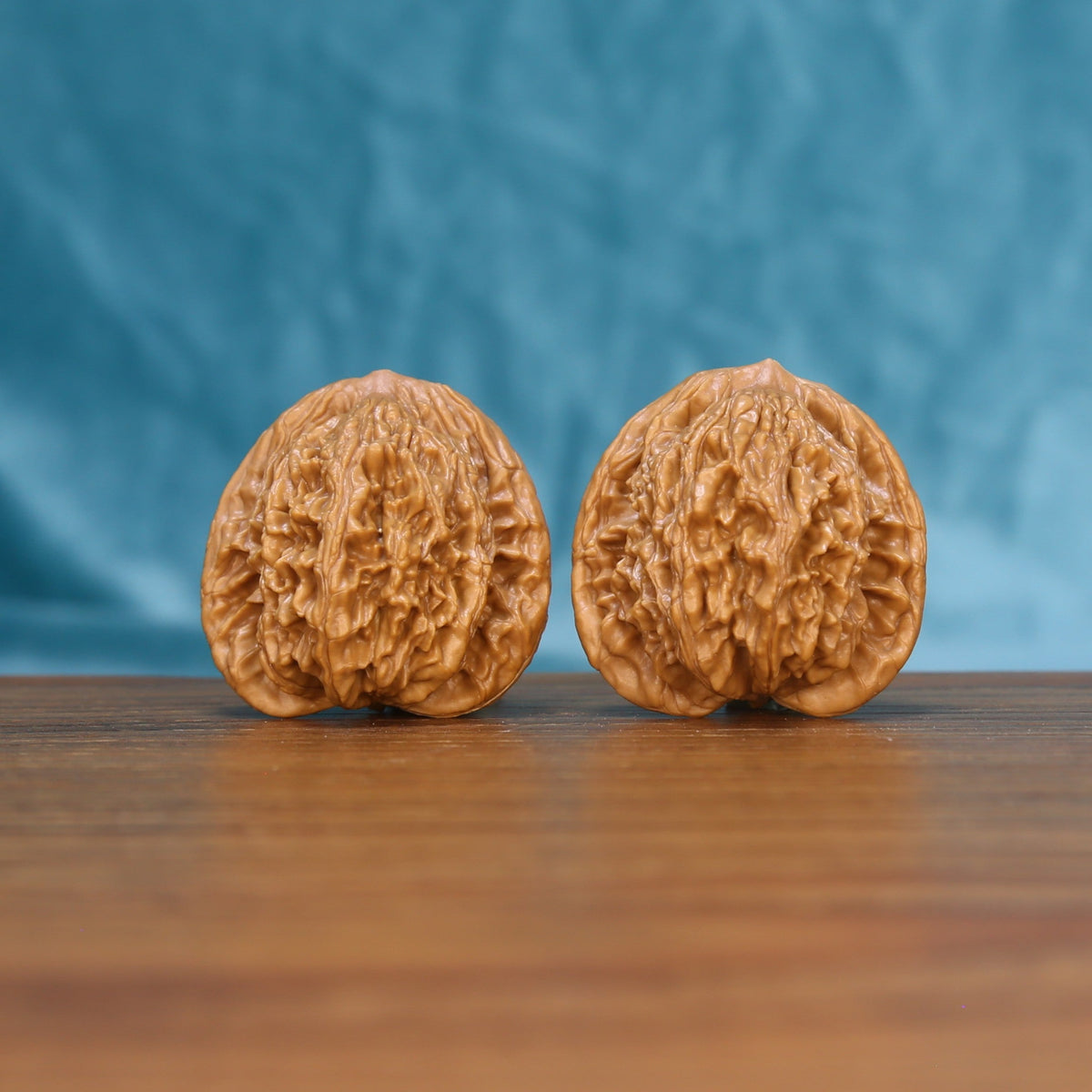 Pair of Wheat Tiger wenwan walnuts with round body and dense relief carving on a wood table against a blue background
