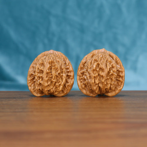 Pair of Wheat Tiger wenwan walnuts with round body and dense relief carving on a wood table against a blue background
