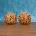 Pair of Pinggu Yuanbao Wenwan walnuts standing upright on a wooden surface against a blue background
