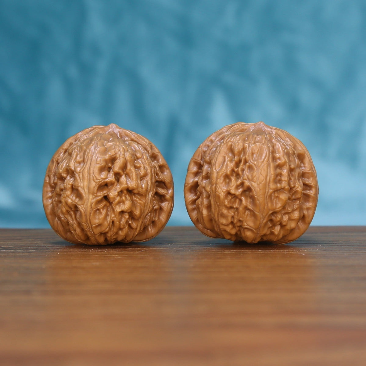 Pair of Pinggu Yuanbao Wenwan walnuts standing upright on a wooden surface against a blue background
