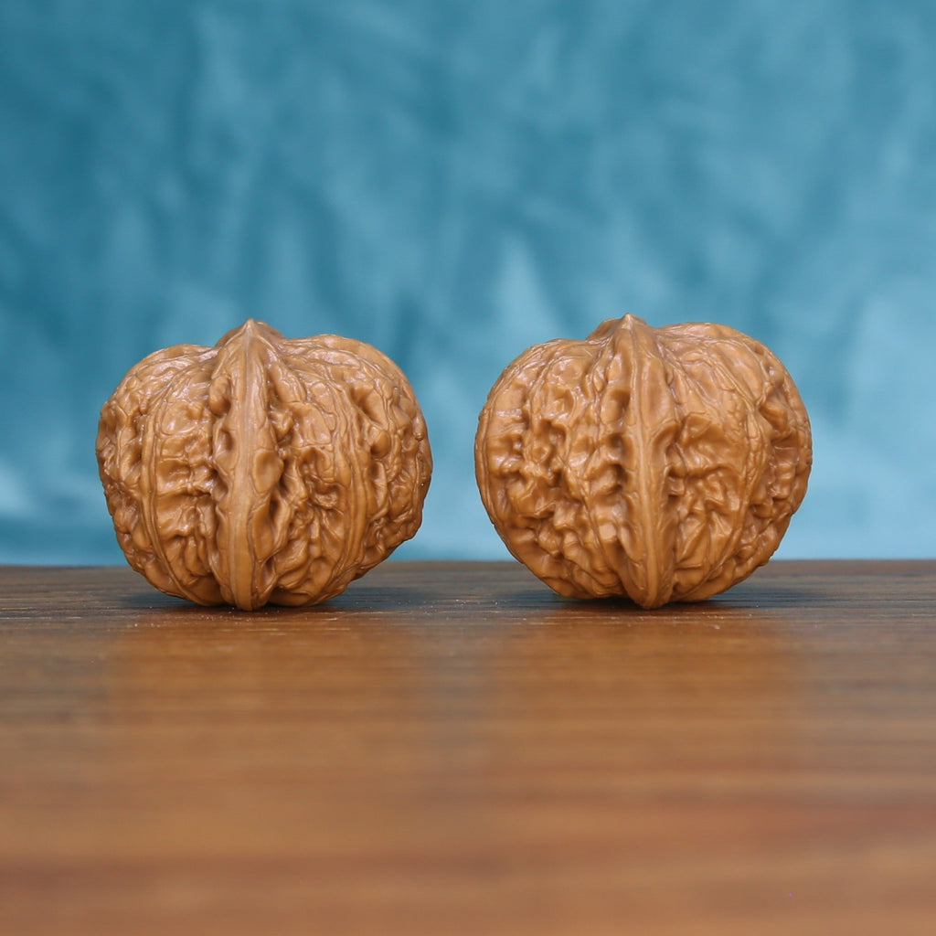 Side view of two Pinggu Yuanbao Wenwan walnuts showing their compact rounded profile
