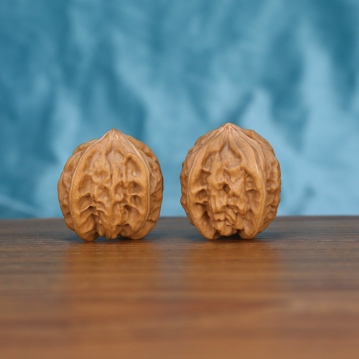 Two Qi-Da-Hai Si-Leng wenwan walnuts on wooden surface, blue fabric background – matching geometric monoliths set