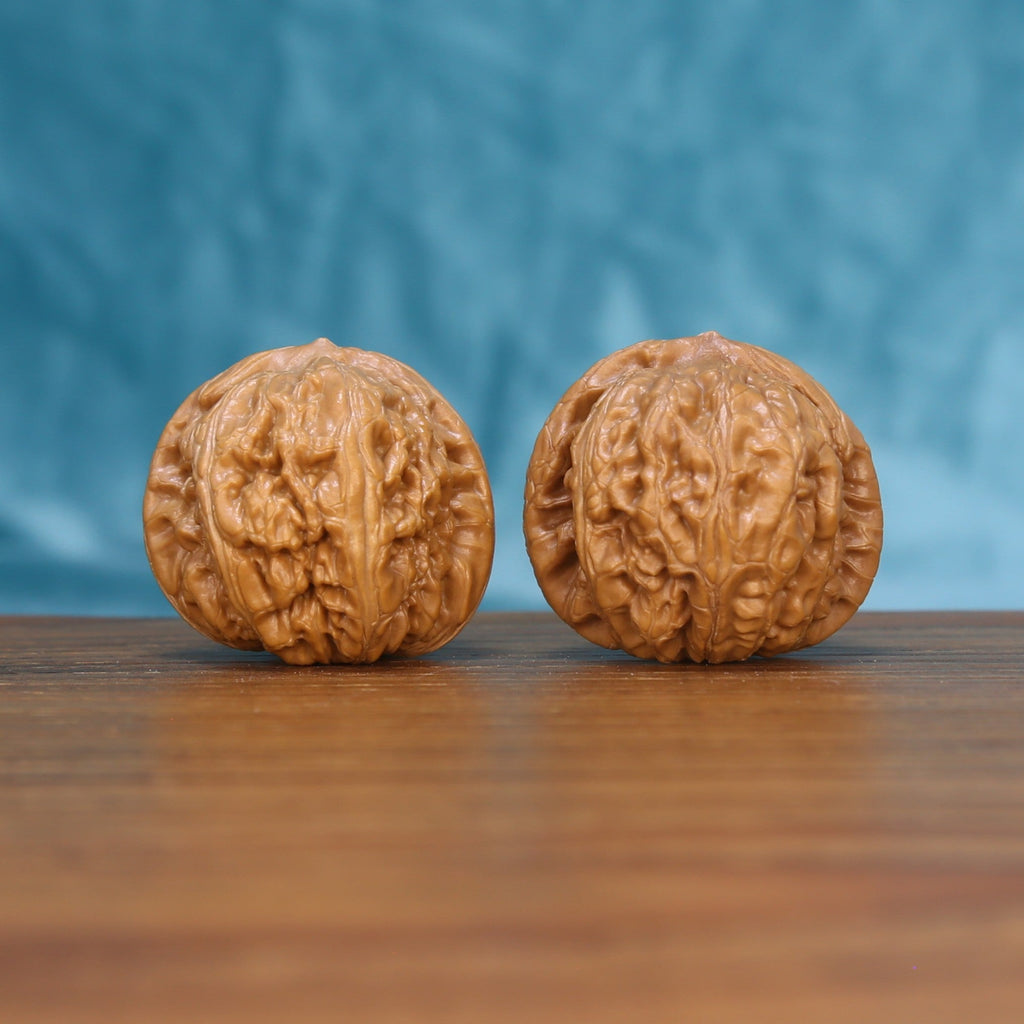 Pair of Pinggu Ingot wenwan walnuts with round full body and dense relief carving on a wood table against a blue background
