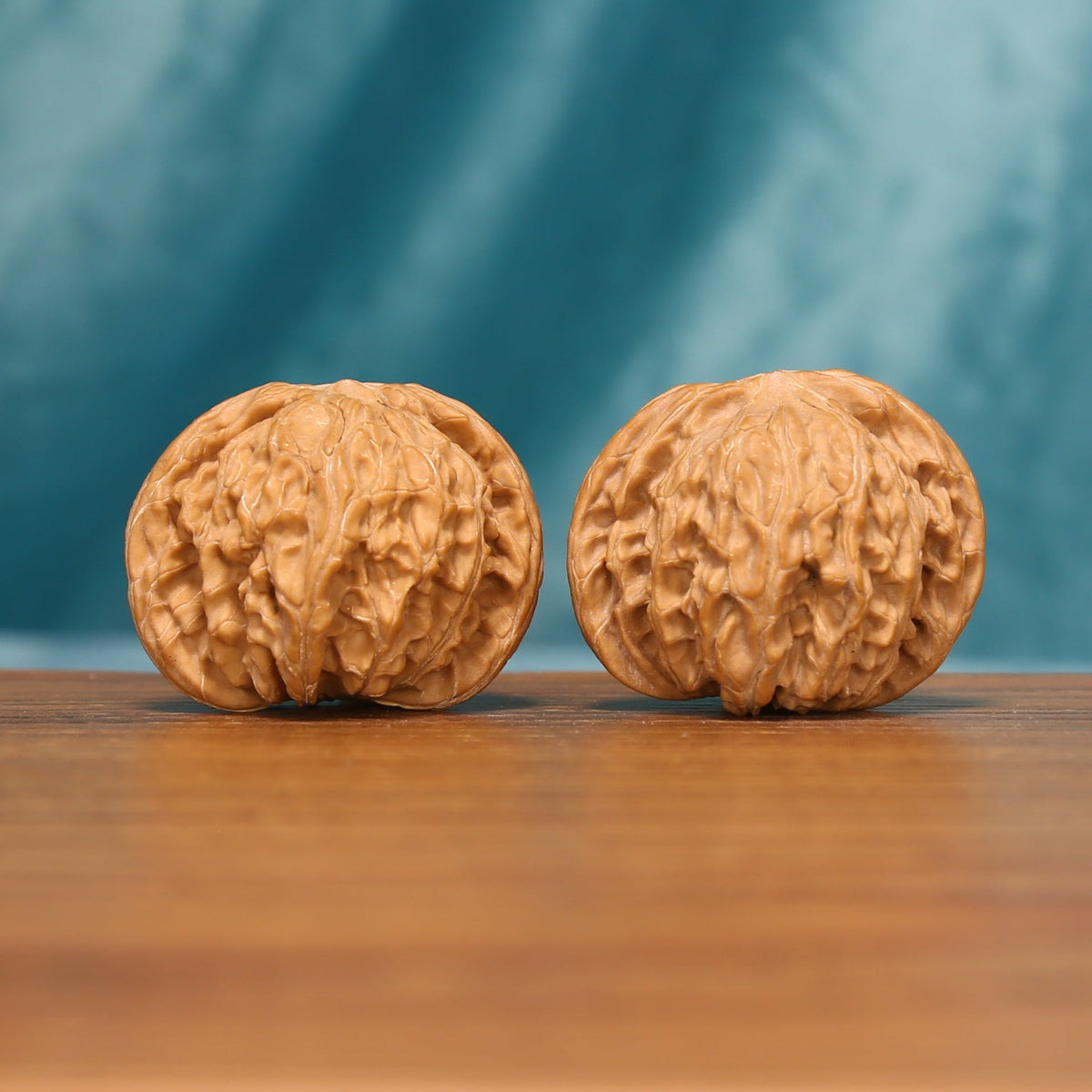 A pair of Carved Millstones Wenwan walnuts shown from the front on a wooden tabletop
