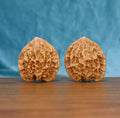 Pair of Emperor wenwan walnuts with tall peach-shaped form and deep relief carving on a wood table against a blue background
