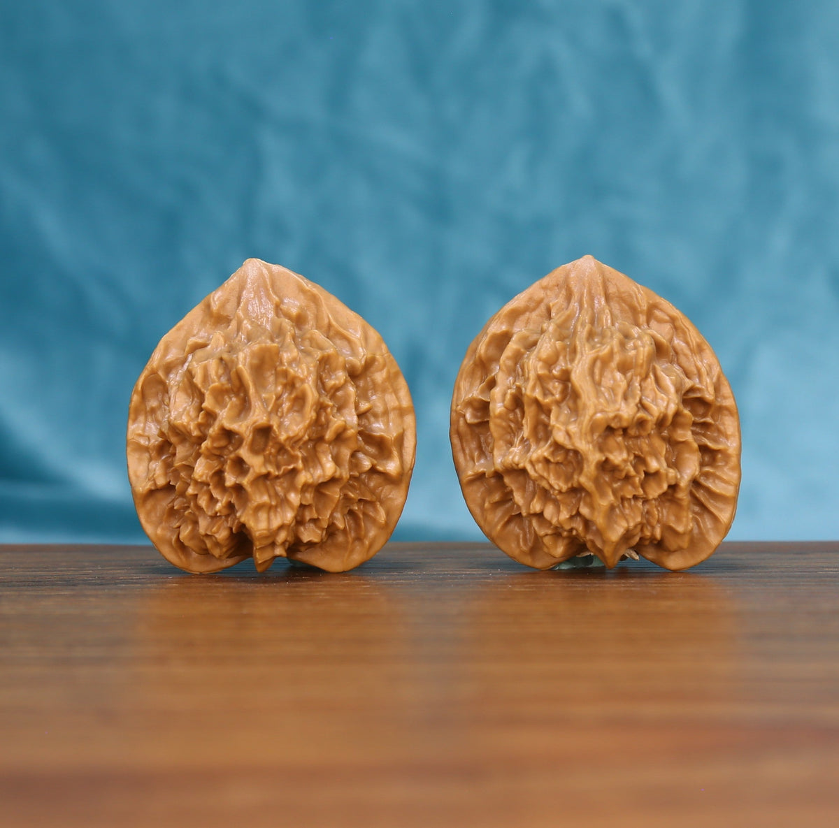 Pair of Emperor wenwan walnuts with tall peach-shaped form and deep relief carving on a wood table against a blue background
