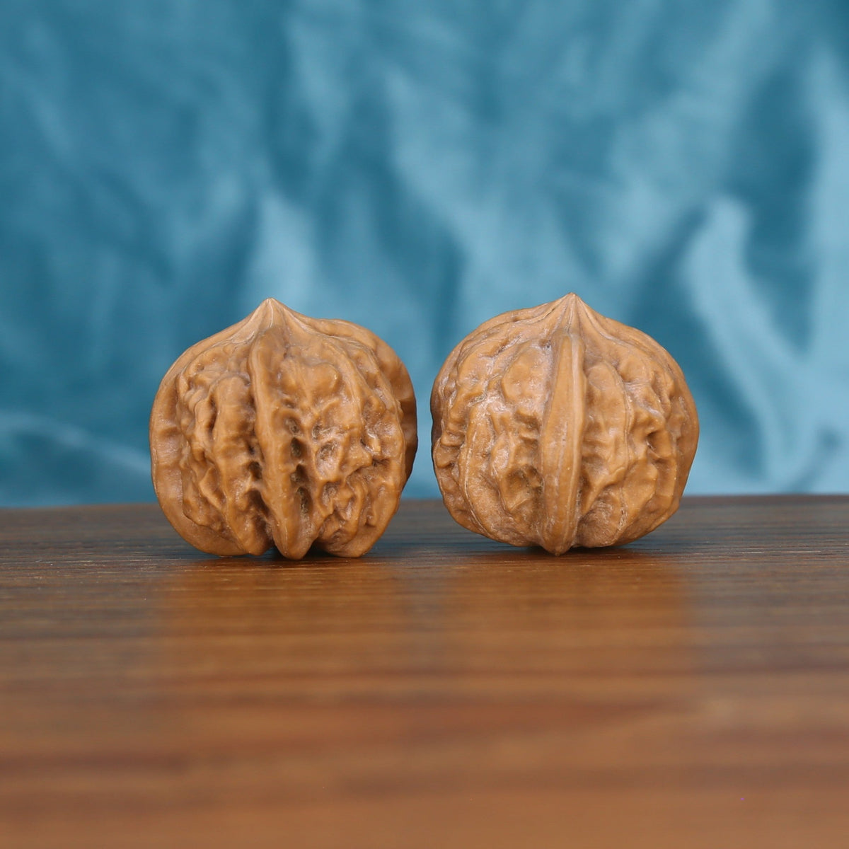Two Qi-Da-Hai San-Leng wenwan walnuts on wooden surface, blue fabric background – matching tri-star geometry set