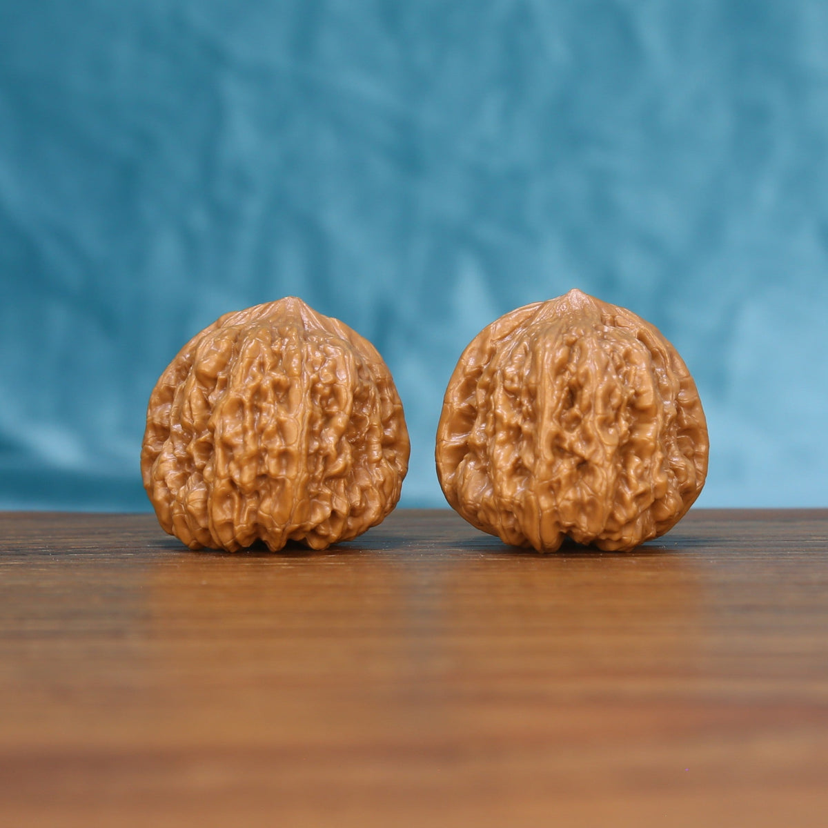 Pair of Pinggu Concave Base Wenwan walnuts standing upright on a wooden surface against a blue background
