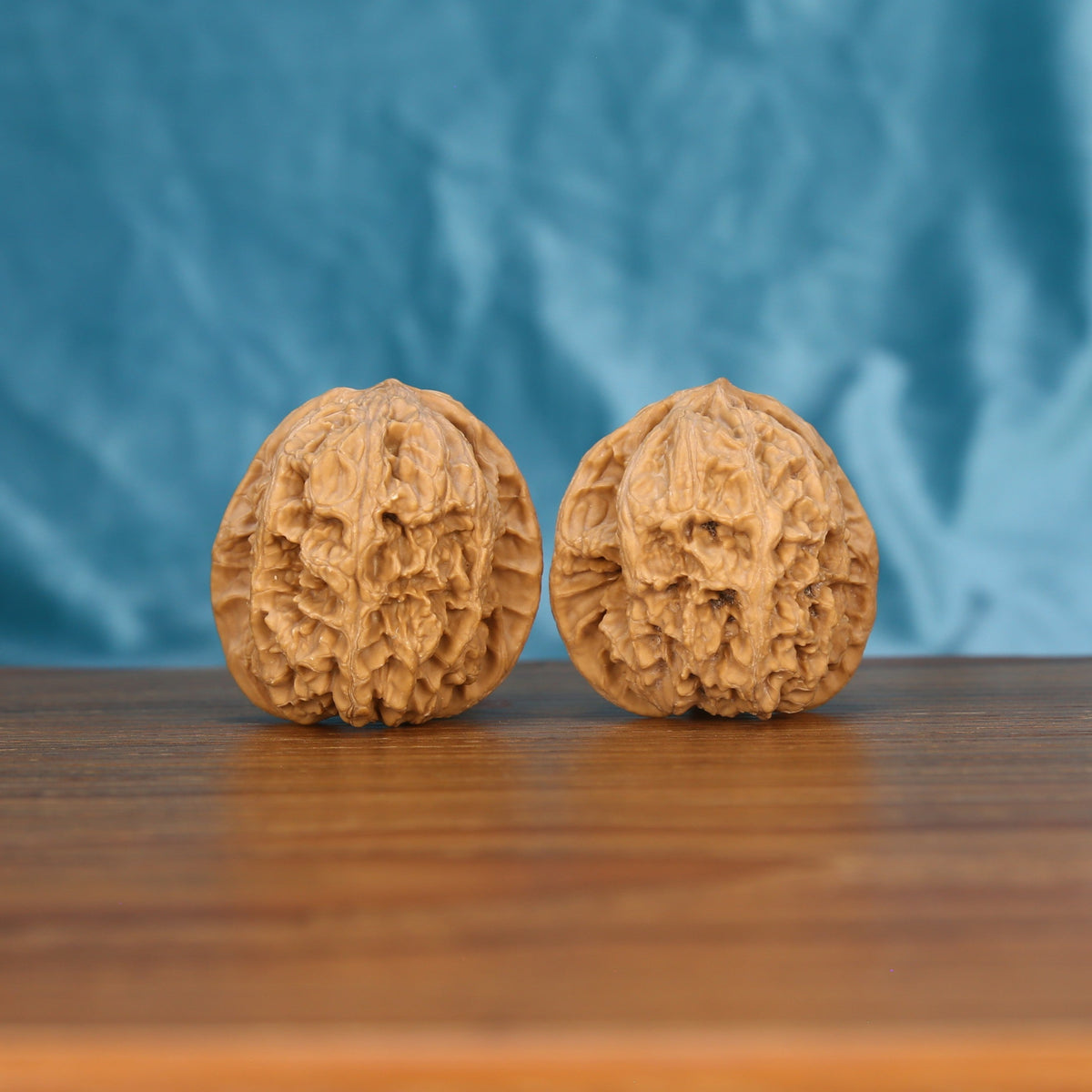 Two premium wenwan walnuts displayed on wooden surface with blue fabric background

